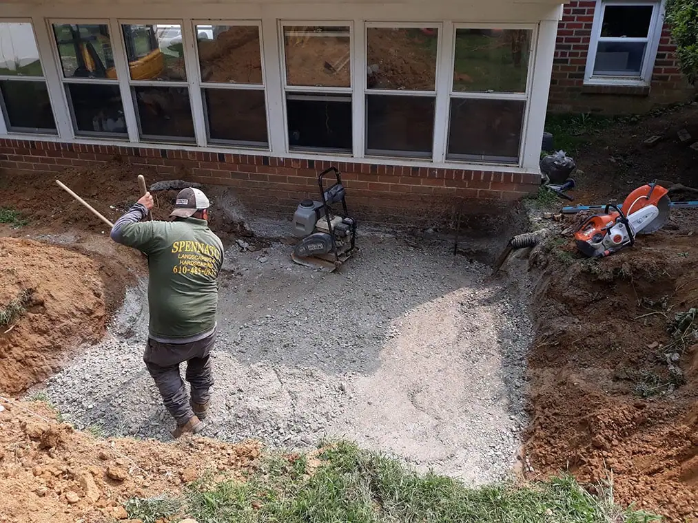 Construction worker in a green shirt is compacting gravel for a new patio or foundation next to a house.